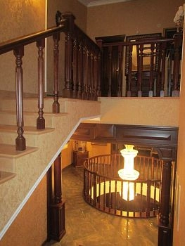 Лестница для загородного дома является важнейшей функциональной составляющей общего дизайна. В данном случае, тёмные перила и балясины гармонично смотрятся с арочными колоннами межэтажных площадок.